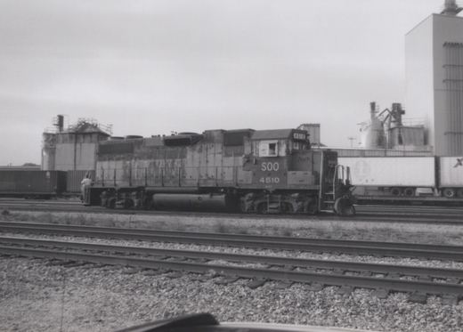 Black and white photo of a Soo Line locomotive numbered 4510 on railroad tracks in a yard, with freight cars and a trailer in the background.