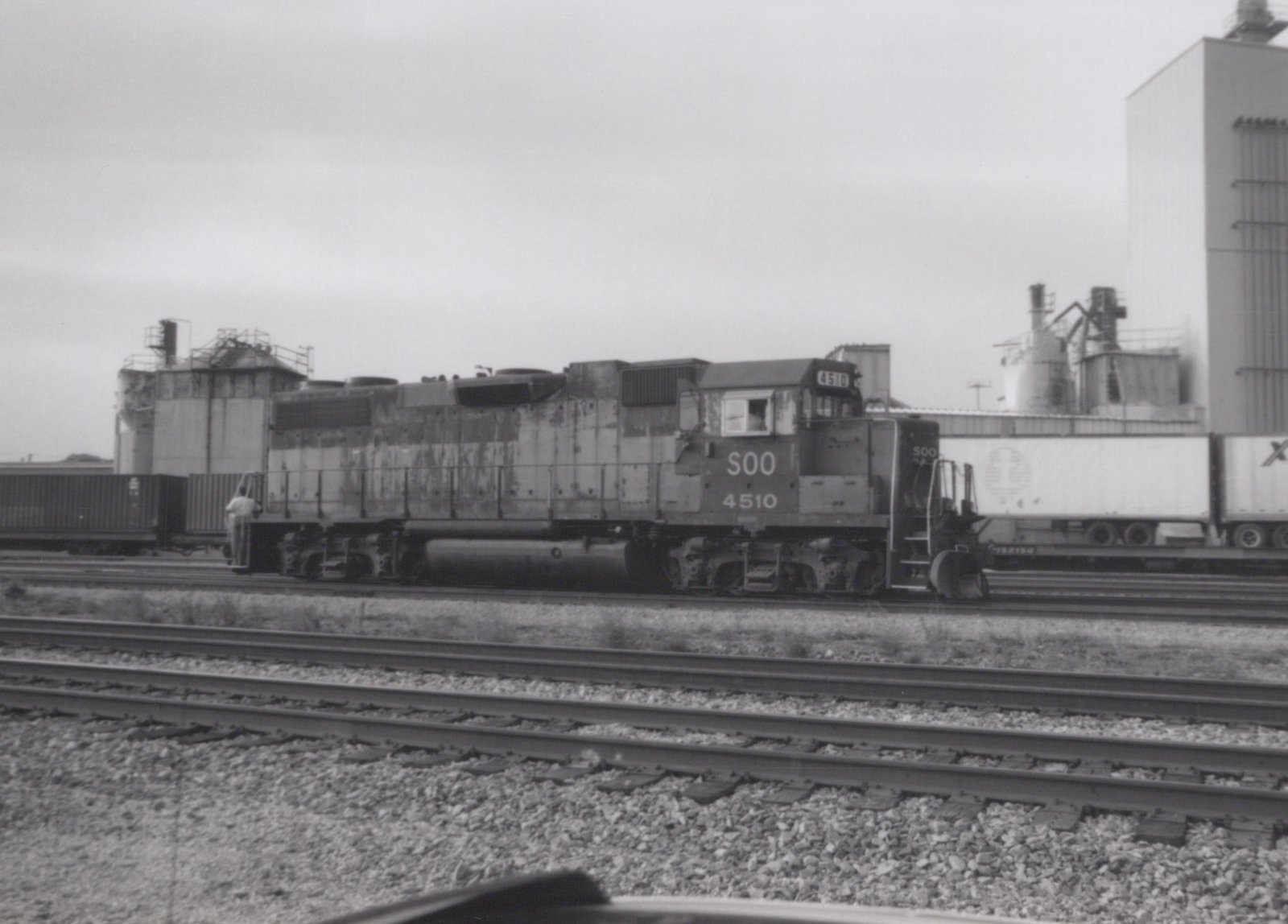 Black and white photo of a Soo Line locomotive numbered 4510 on railroad tracks in a yard, with freight cars and a trailer in the background.