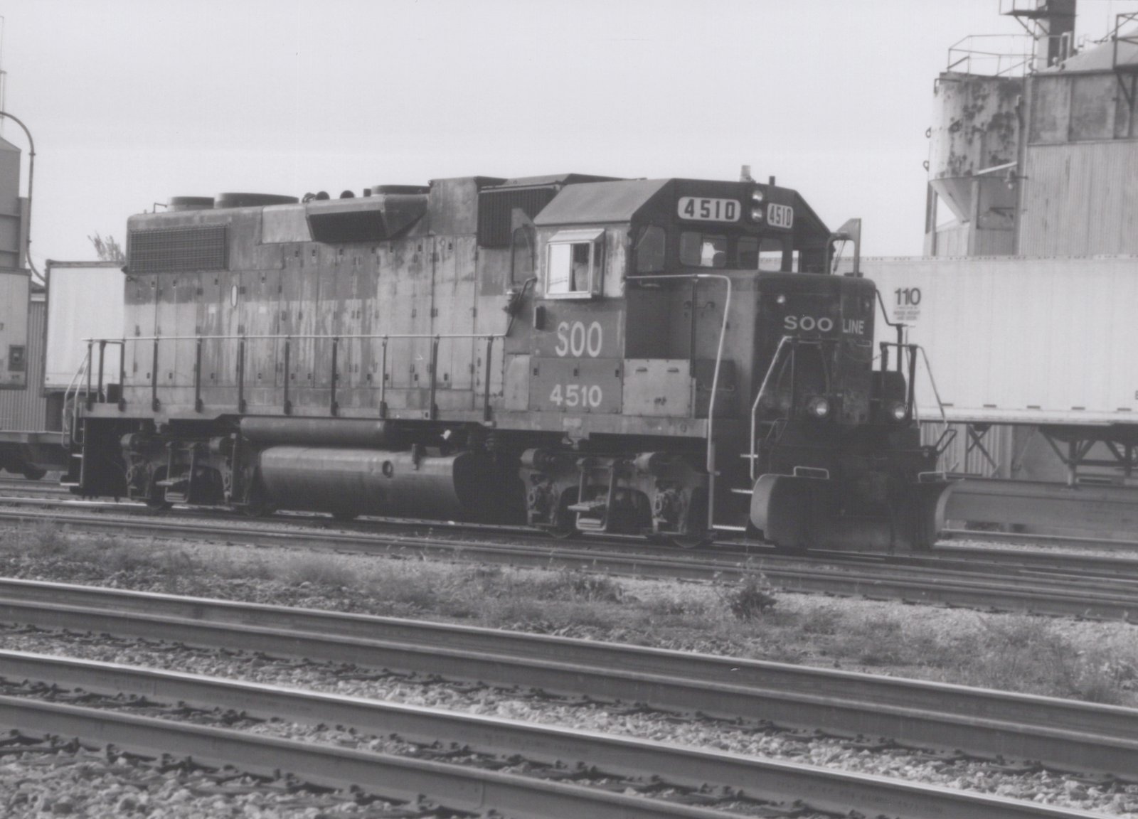 A SOO Line diesel locomotive, number 4510, stands on railroad tracks in a yard with a freight car behind it.