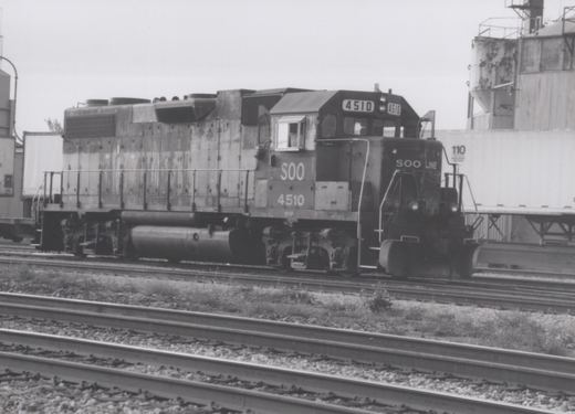 A SOO Line diesel locomotive, number 4510, stands on railroad tracks in a yard with a freight car behind it.
