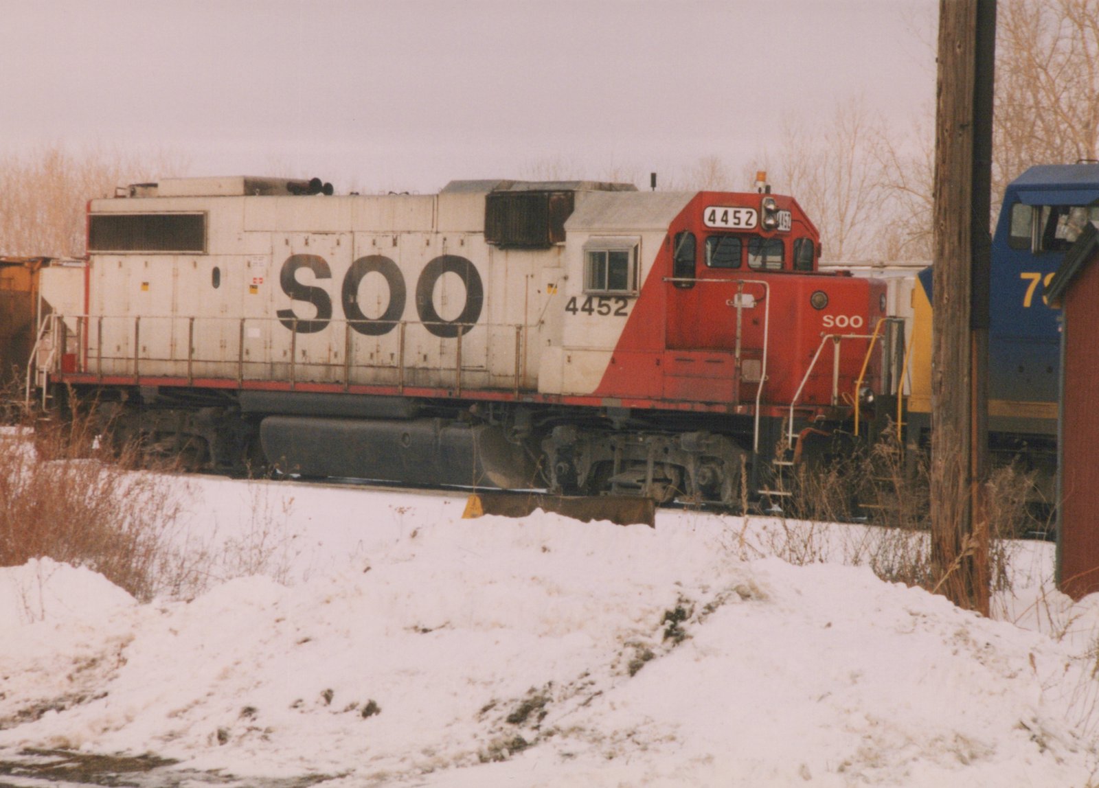 A side view of a SOO Line diesel locomotive number 4452, painted white with a red nose, standing on railroad tracks with snow on the ground.