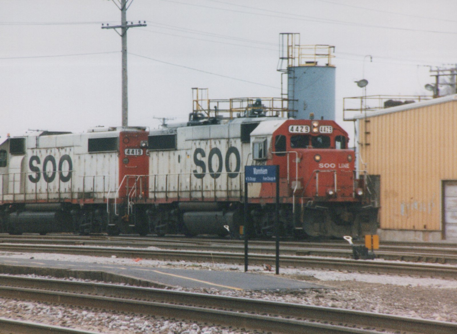 Two SOO Line diesel locomotives, numbers 4429 and 4419, are stopped at the Mannheim station platform on a cloudy day with snow on the ground.
