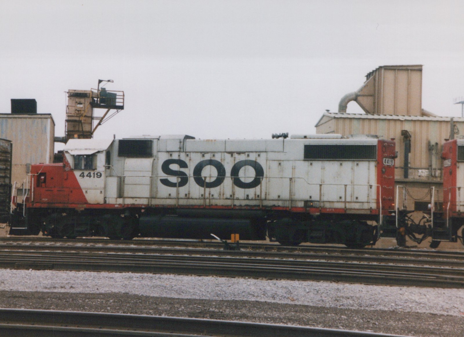 A white and red SOO Line diesel locomotive, number 4419, is shown in profile on a set of tracks in a rail yard with snow on the ground.