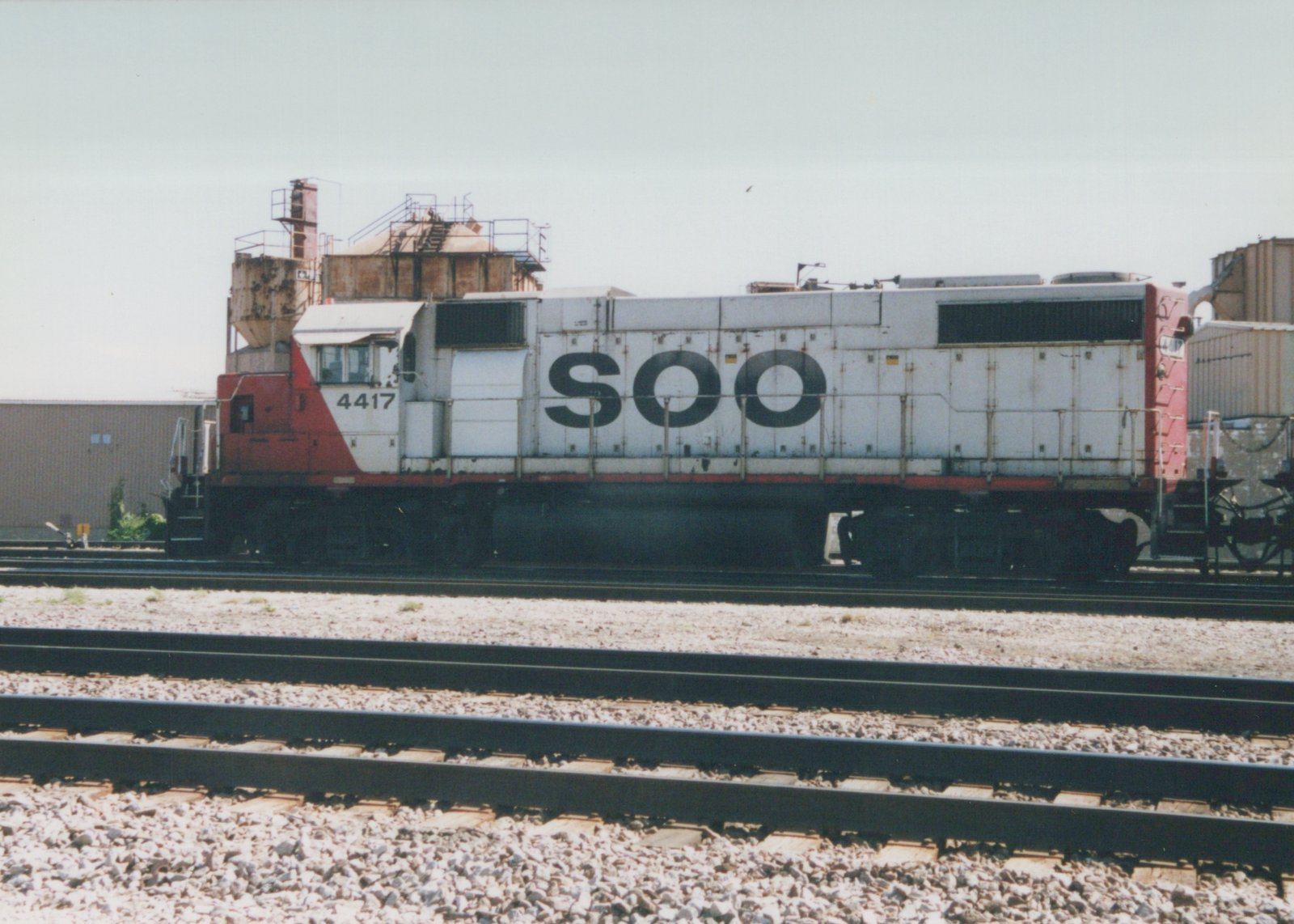 Side view of a white and red Soo Line diesel locomotive numbered 4417 on a gravel track in a railroad yard under an overcast sky.