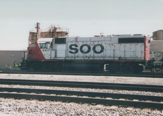 Side view of a white and red Soo Line diesel locomotive numbered 4417 on a gravel track in a railroad yard under an overcast sky.