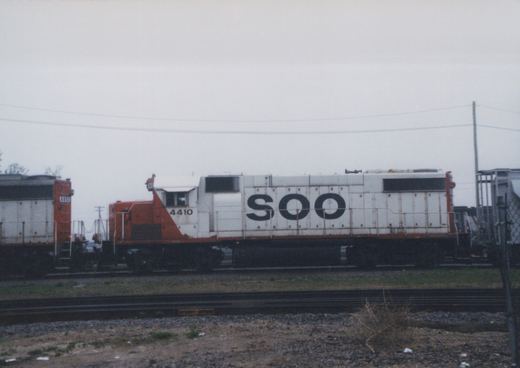 Two SOO Line diesel locomotives, numbered 4410 and 4451, sit side-by-side on tracks in a yard on a cloudy day.