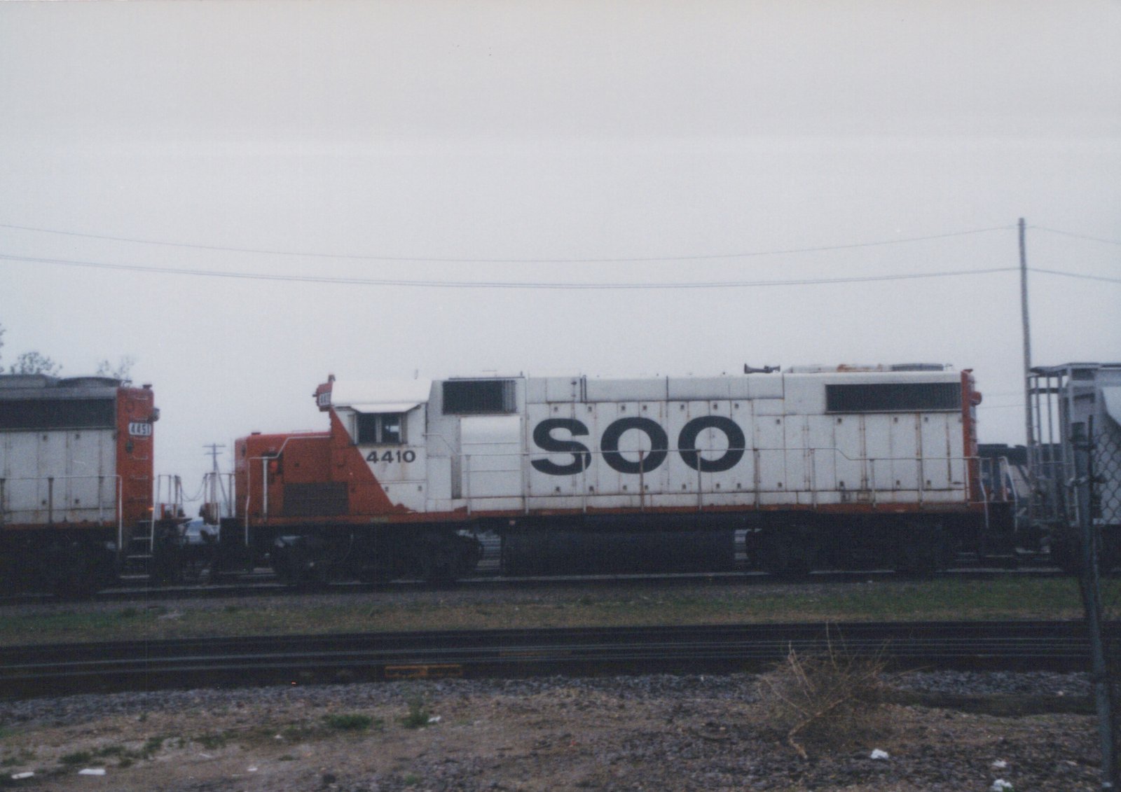 Two SOO Line diesel locomotives, numbered 4410 and 4451, sit side-by-side on tracks in a yard on a cloudy day.