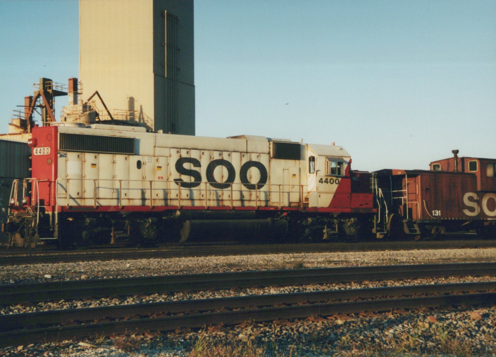A Soo Line EMD SD40-2 diesel locomotive, numbered 4400, stands coupled to a red caboose, numbered 131, on a set of railroad tracks under a clear blue sky.