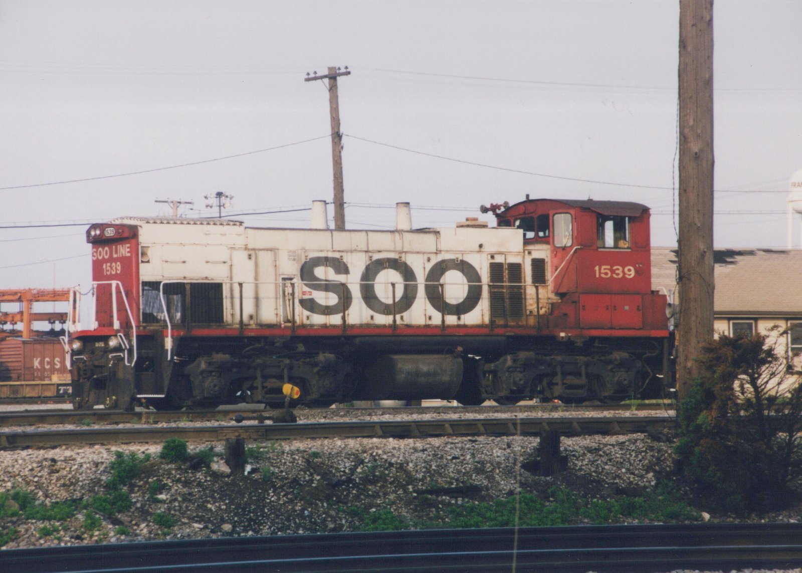 Side view of a red and white SOO Line diesel locomotive number 1539 on railroad tracks, with a water tower and freight cars in the background.
