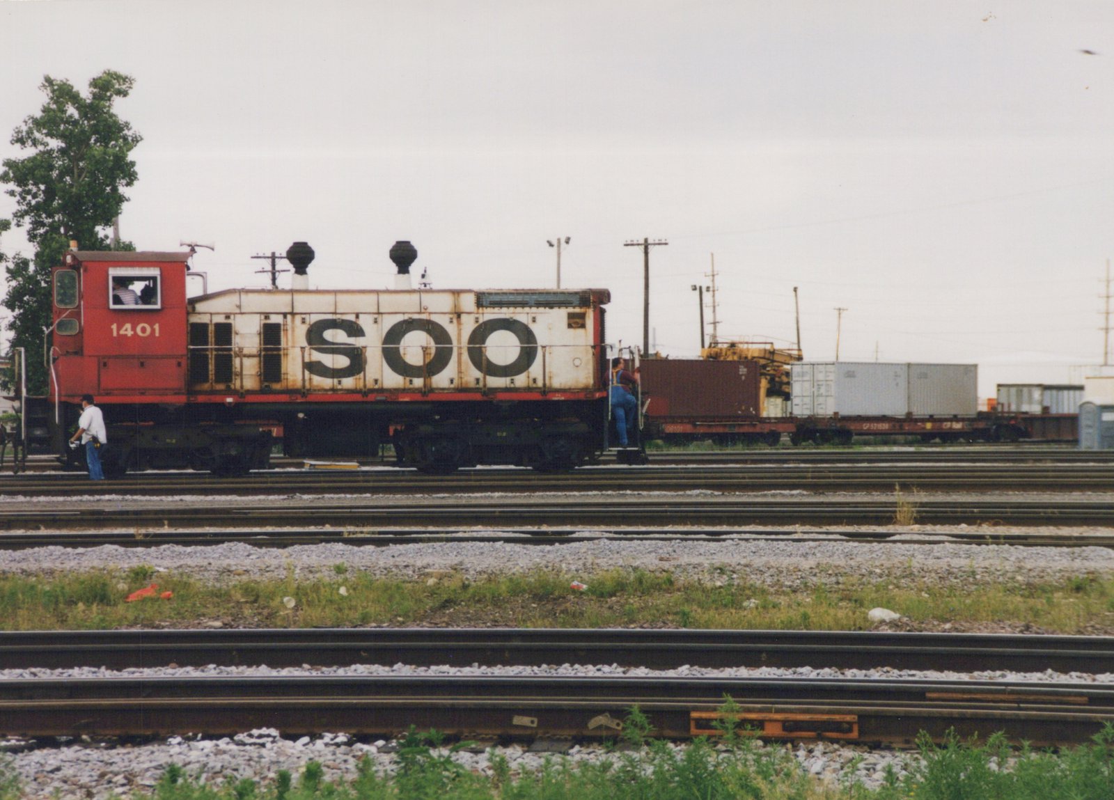 Side view of a SOO Line GP38-2 diesel locomotive numbered 1401 in a rail yard with crew members present and freight cars in the background.