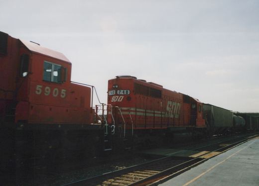 Two red diesel locomotives, one with the SOO Line logo and number 748, on parallel tracks in a yard under an overcast sky.