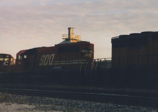 A red SOO Line diesel locomotive, number 748, is shown from a three-quarter front view in a railroad yard at dusk, with its side and front numbers clearly visible. A second locomotive with CP lettering is partially seen to the left.