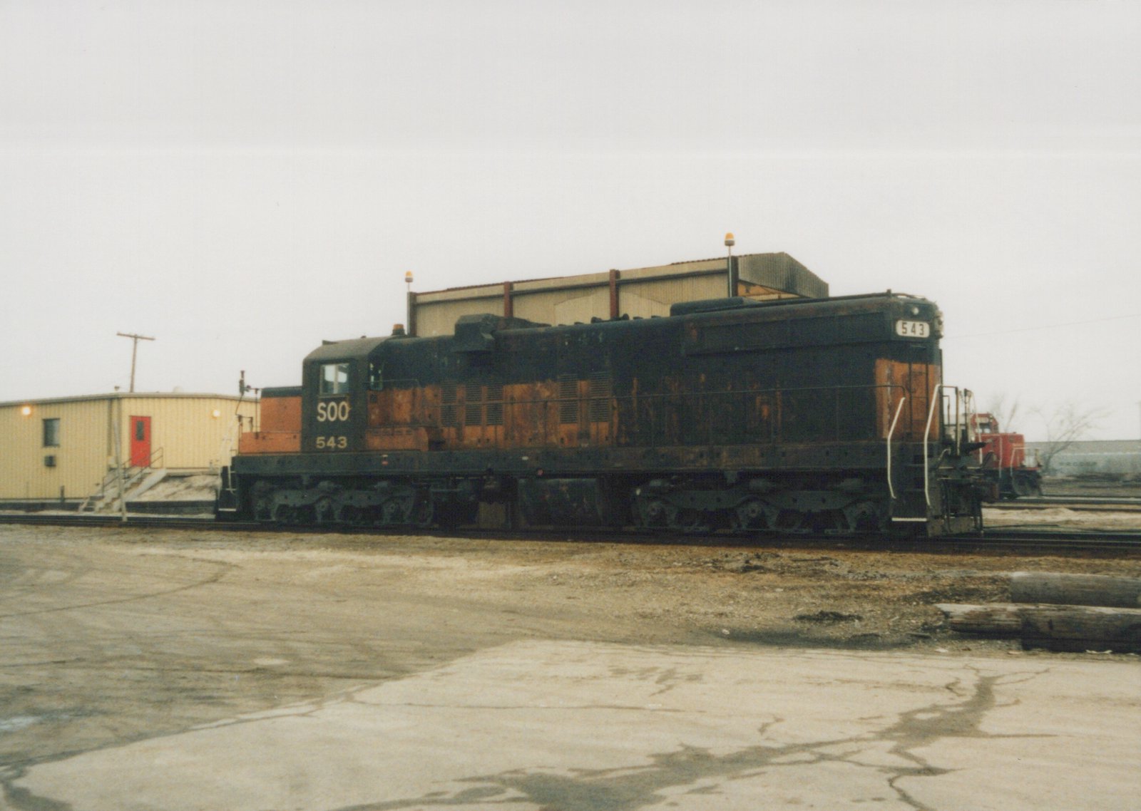 A side view of a black and orange Soo Line diesel locomotive numbered 543, parked on tracks in a gravel and concrete yard with overcast skies.