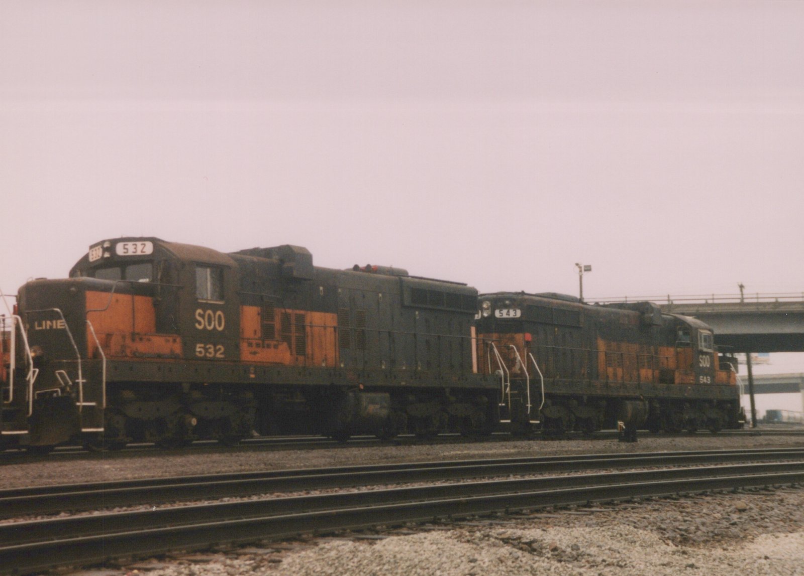 Side view of two black and orange Soo Line diesel locomotives, numbers 532 and 543, coupled on a set of tracks in a rail yard on a cloudy day.