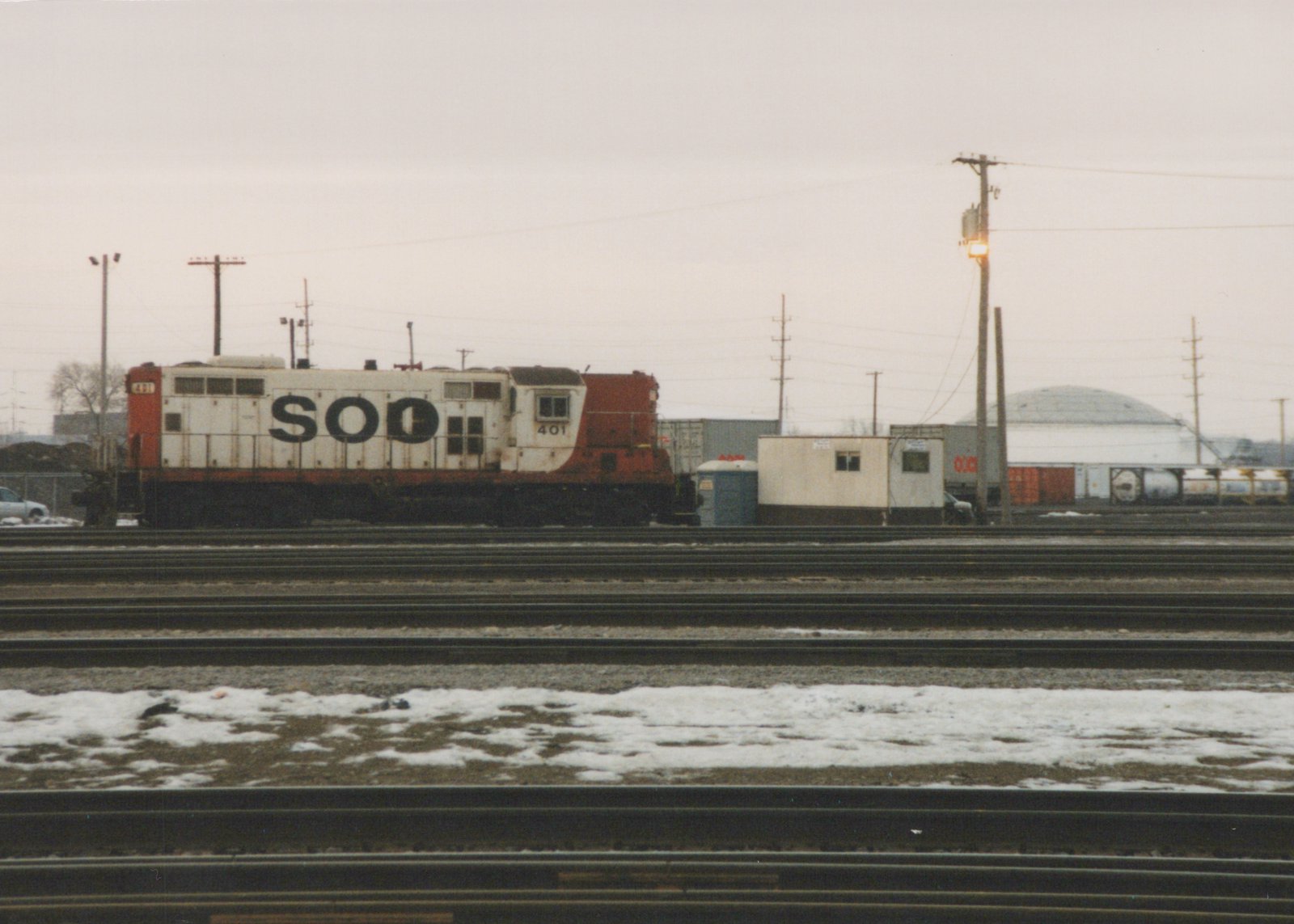 A white and orange-red Soo Line diesel locomotive with number 401, parked on multiple tracks in a snowy rail yard under an overcast sky.