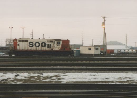 A white and orange-red Soo Line diesel locomotive with number 401, parked on multiple tracks in a snowy rail yard under an overcast sky.
