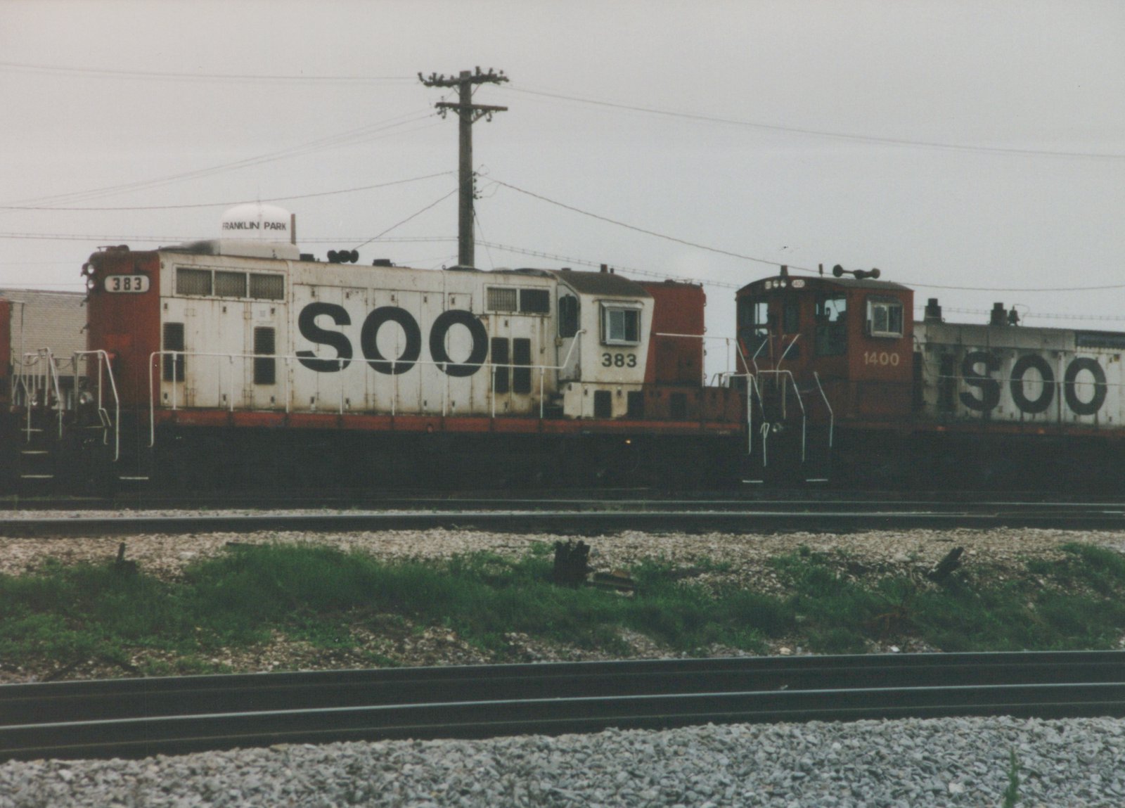 Two white and red SOO Line diesel locomotives, numbered 383 and 1400, are parked on parallel tracks in Franklin Park, Illinois, with a water tower visible in the background.