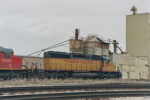 A yellow Union Pacific locomotive numbered 3680 and a red Illinois Central locomotive numbered 6125 sit on parallel tracks in an industrial yard under an overcast sky.
