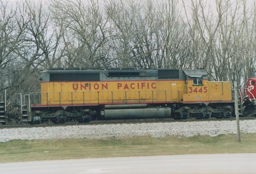 A yellow Union Pacific diesel locomotive with the number 3445 on its side and front, sitting on railroad tracks with bare trees in the background.