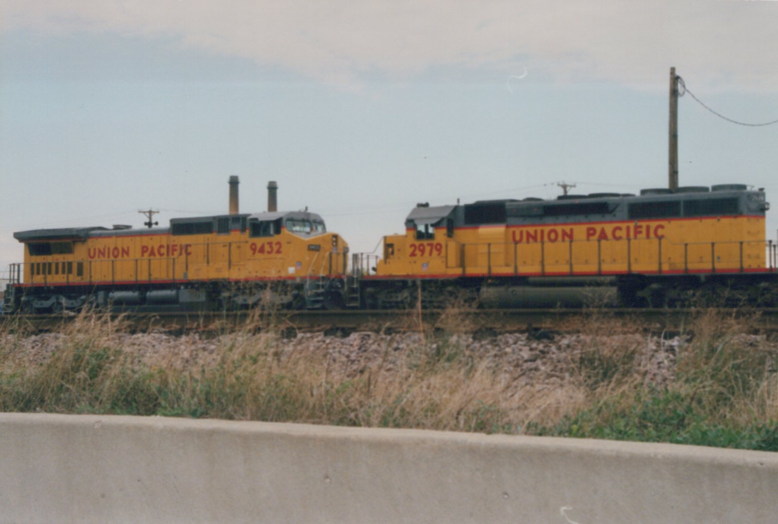 Two yellow Union Pacific diesel locomotives, numbered 9432 and 2979, are traveling on a railroad track under an overcast sky.