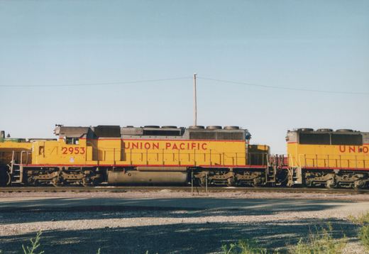 Side view of two yellow and red Union Pacific locomotives, numbered 2953 and 2954, standing on parallel tracks in a sunny, open yard.