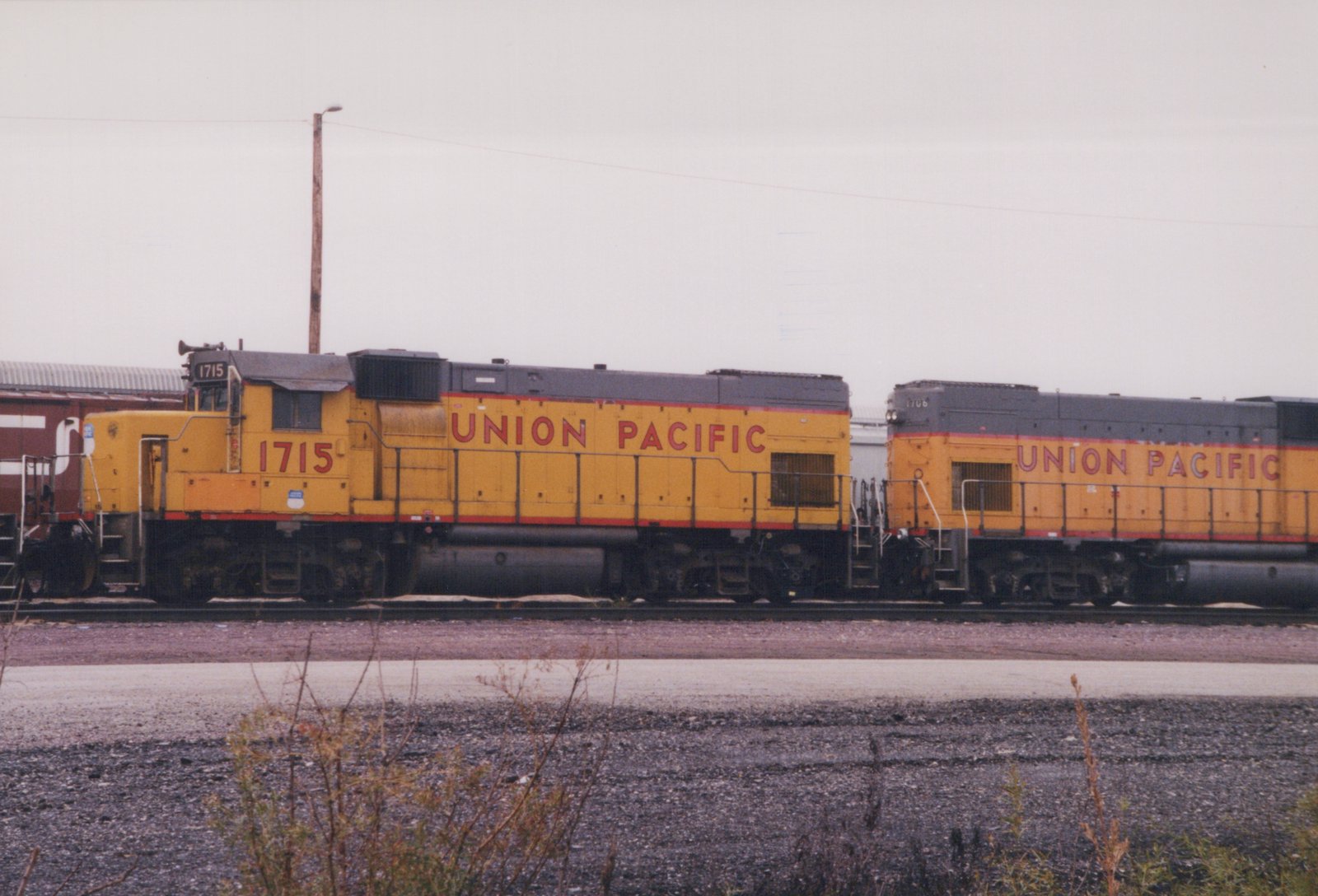 Two yellow Union Pacific locomotives, numbers 1715 and 1706, are parked side by side in a railroad yard on an overcast day.