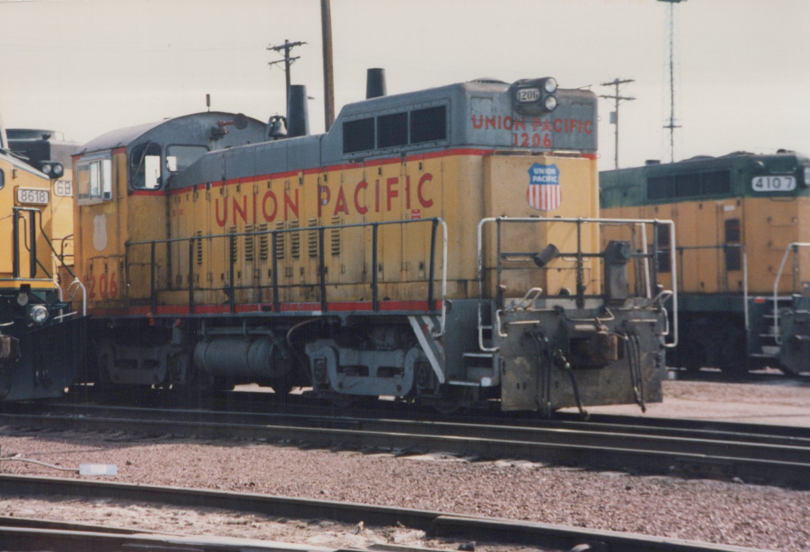 A yellow and gray Union Pacific diesel locomotive numbered 1206 is parked in a yard, with two other locomotives nearby.