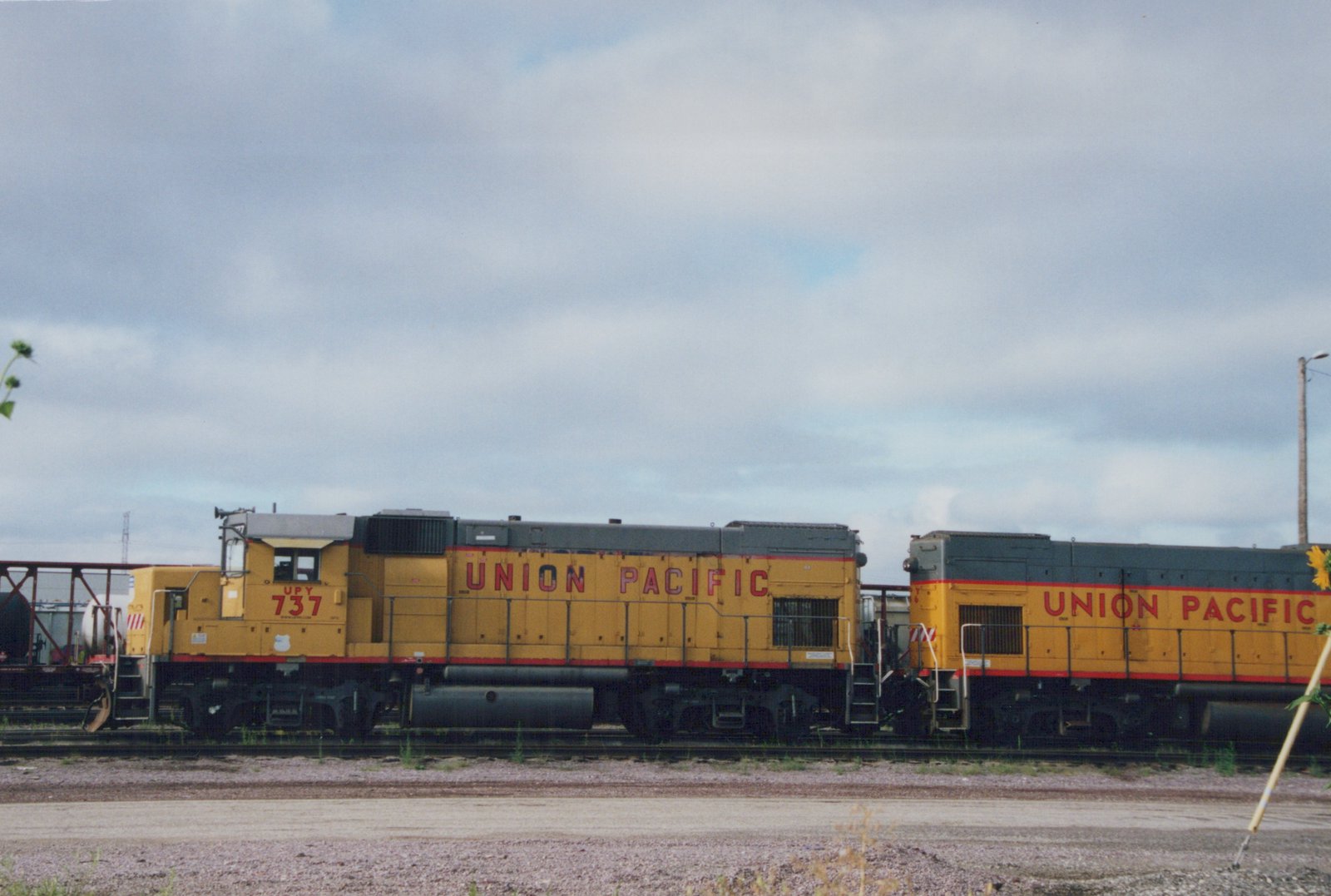 Two yellow Union Pacific diesel locomotives, including number 737, are parked side-by-side in a gravel yard under an overcast sky.