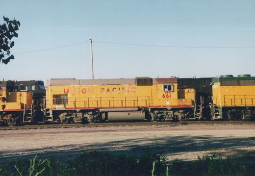 A yellow Union Pacific diesel locomotive numbered 661 sits on tracks in a rail yard under a clear sky.