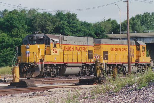Two yellow Union Pacific locomotives, numbered Y554 and 550, are parked side-by-side on a railroad track in a yard, with trees and an overpass in the background.