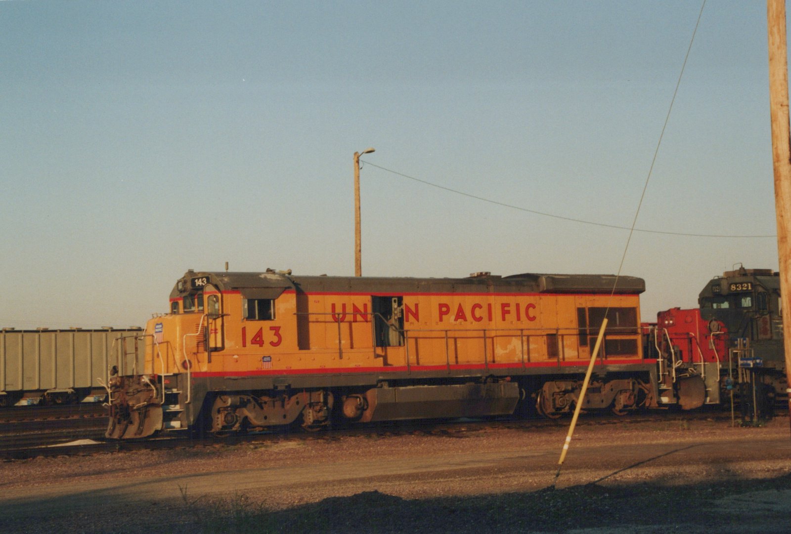 A yellow Union Pacific diesel locomotive numbered 143 on a railroad track in a yard, with another locomotive numbered 8321 visible behind it.