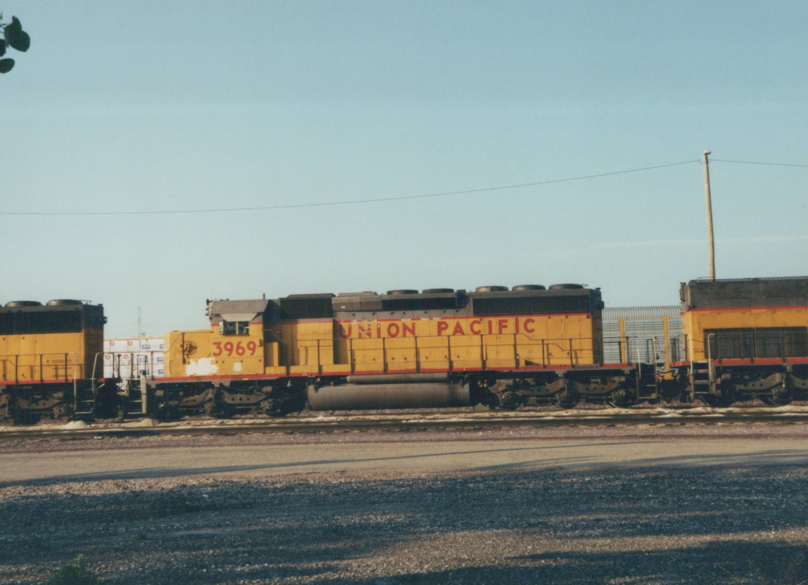Side view of a yellow Union Pacific freight locomotive numbered 3969, with another similar locomotive behind it, on tracks at a rail yard under a clear sky.
