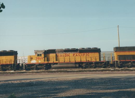 Side view of a yellow Union Pacific freight locomotive numbered 3969, with another similar locomotive behind it, on tracks at a rail yard under a clear sky.
