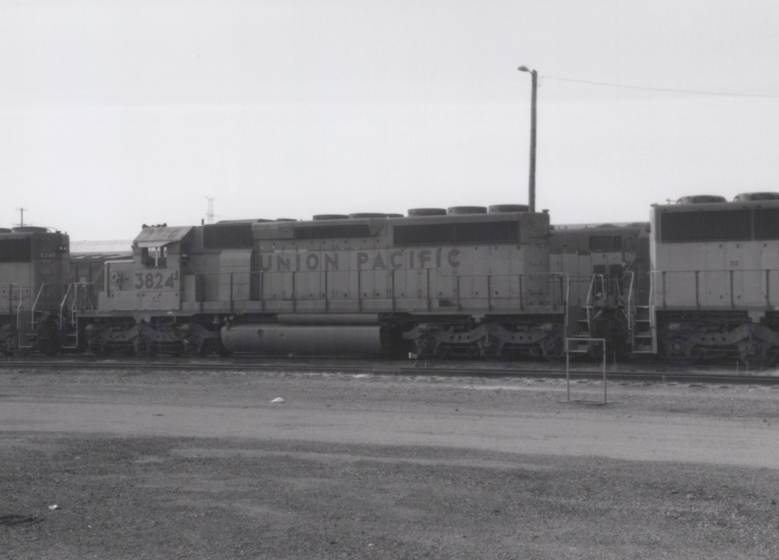Side view of a Union Pacific GP38-2 diesel locomotive numbered 3824, parked in a gravel rail yard with another locomotive visible to the left.