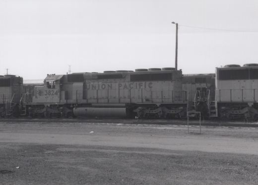 Side view of a Union Pacific GP38-2 diesel locomotive numbered 3824, parked in a gravel rail yard with another locomotive visible to the left.