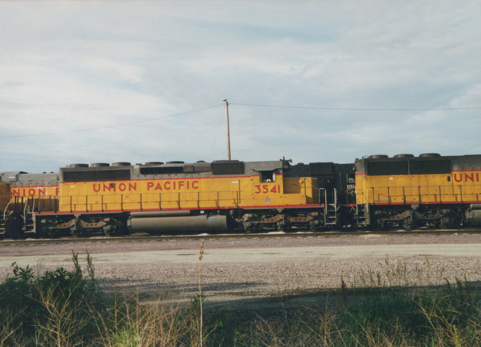 Side view of a yellow and red Union Pacific locomotive, number 3541, on a railroad track under an overcast sky.