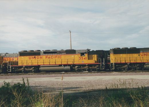Side view of a yellow and red Union Pacific locomotive, number 3541, on a railroad track under an overcast sky.