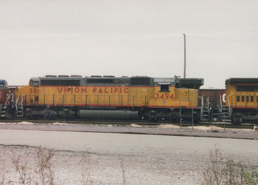 A yellow Union Pacific diesel locomotive with the number 3494 is parked on tracks in a snowy yard under an overcast sky.