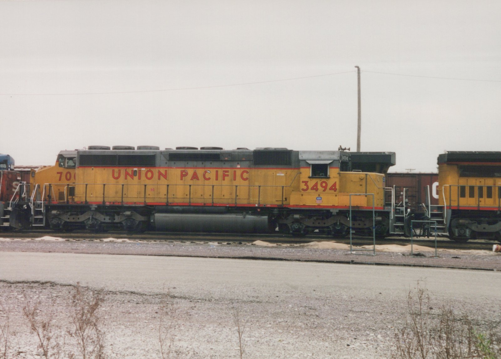 A yellow Union Pacific diesel locomotive with the number 3494 is parked on tracks in a snowy yard under an overcast sky.
