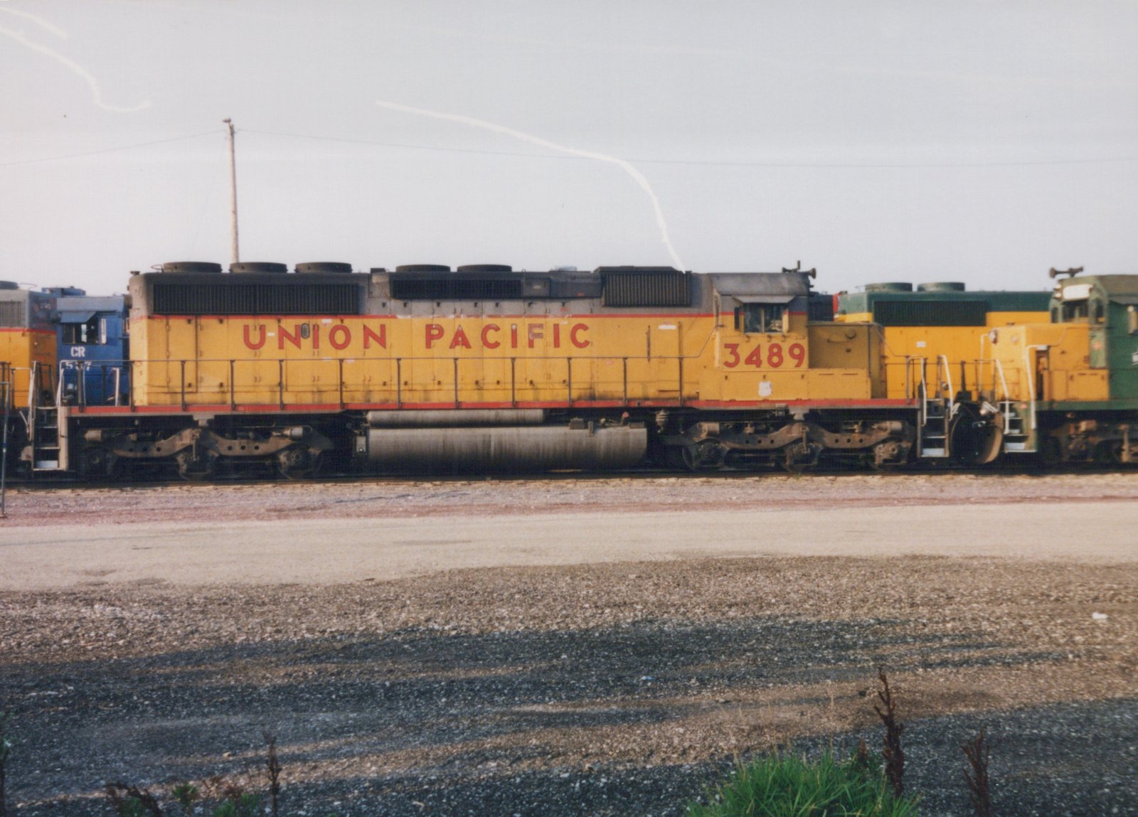 A side view of a yellow and red Union Pacific diesel locomotive number 3489 in a railroad yard, with other locomotives visible nearby.