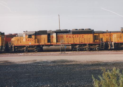 Side view of a yellow Union Pacific locomotive numbered 3422 standing in a rail yard, with another locomotive visible behind it.