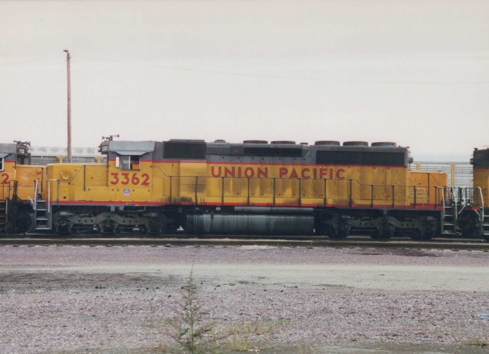 Side view of a yellow Union Pacific diesel locomotive with the number 3362, parked on tracks in a gravel yard under an overcast sky.
