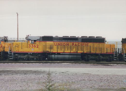 Side view of a yellow Union Pacific diesel locomotive with the number 3362, parked on tracks in a gravel yard under an overcast sky.