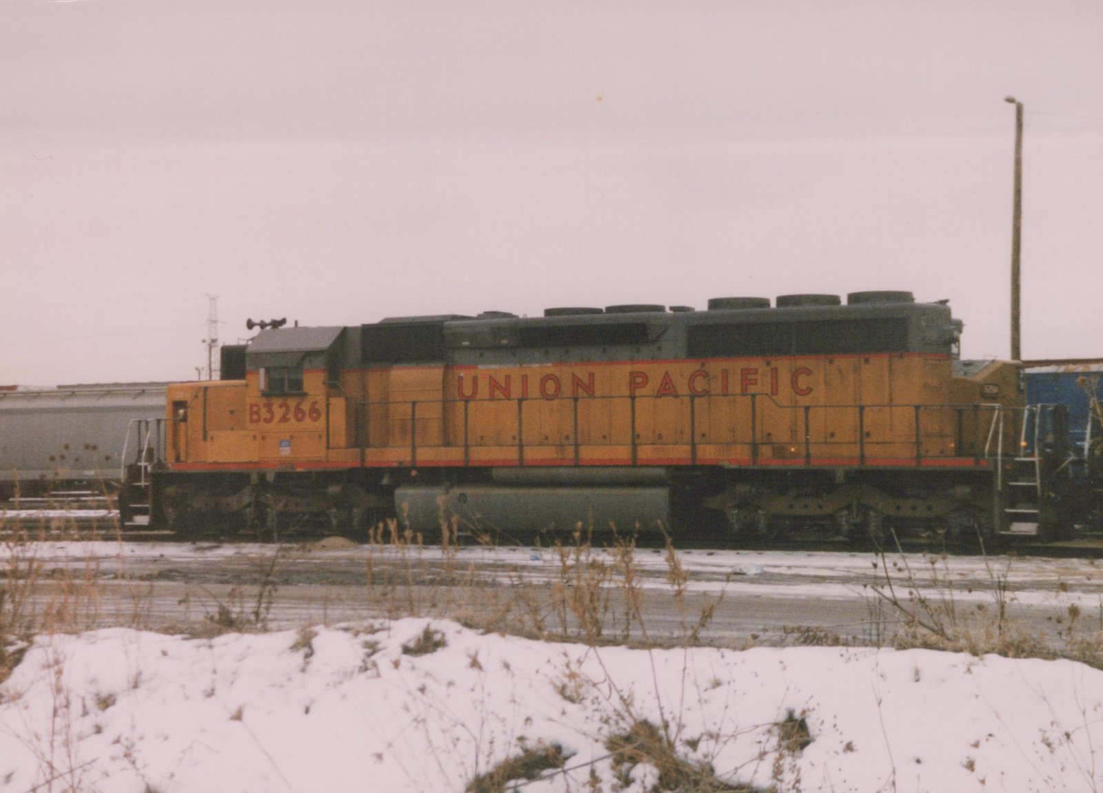 A yellow and gray Union Pacific diesel locomotive numbered B3266 is parked on railroad tracks with snow covering the ground in the foreground.