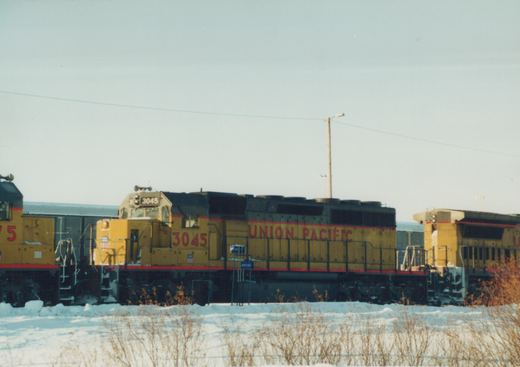 A yellow and black Union Pacific locomotive, number 3045, is parked on a snow-covered track with another locomotive partially visible behind it.