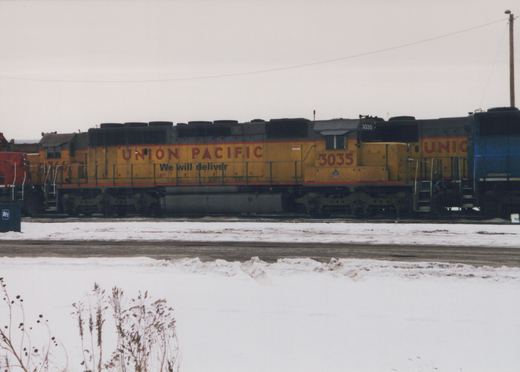 A yellow Union Pacific diesel locomotive with the number 3035 is parked on a snow-covered track in a railyard.