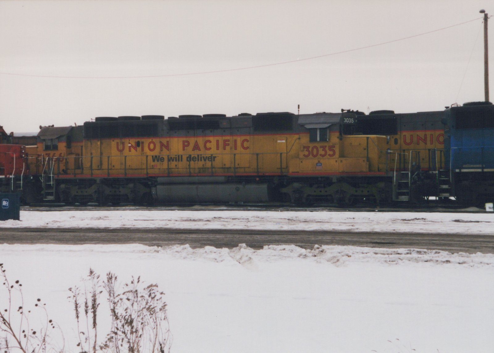 A yellow Union Pacific diesel locomotive with the number 3035 is parked on a snow-covered track in a railyard.
