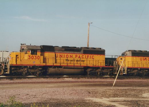 Two yellow Union Pacific diesel locomotives, numbered 3030 and 2986, are parked side by side in a gravel yard under a clear sky.