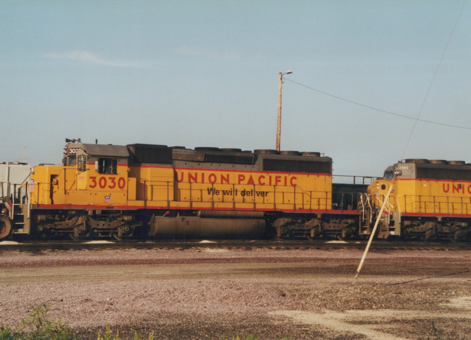 Two yellow Union Pacific diesel locomotives, numbered 3030 and 2986, are parked side by side in a gravel yard under a clear sky.