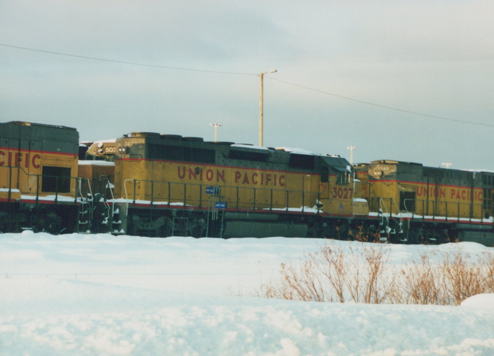 Three Union Pacific diesel locomotives, including #3027, are parked in a snow-covered yard under an overcast sky.